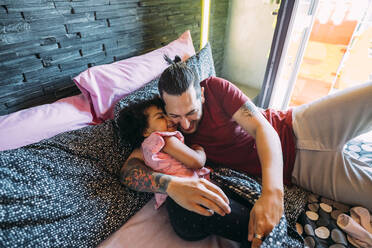 Playful father and daughter lying on bed at home - MEUF01920