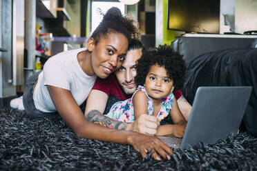 Parents with daughter using laptop while lying on rug at home - MEUF01929