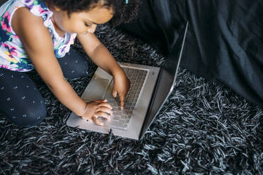 Baby-Mädchen mit Laptop kniend auf Teppich zu Hause - MEUF01930