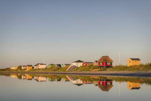 Dänemark, Region Süddänemark, Marstal, Klarer Himmel über einer Reihe von Badehäusern, die sich im Küstenwasser spiegeln - KEBF01572