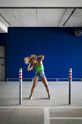Junge Frau tanzt vor einer blauen Wand in einer Unterführung - MAUF03511