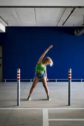 Junge Frau tanzt vor einer blauen Wand in einer Unterführung - MAUF03512