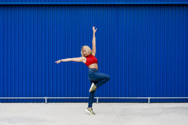 Young woman dancing in front of blue wall in the city - MAUF03518