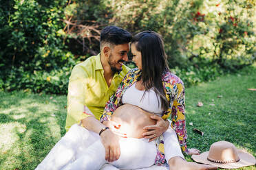 Glücklicher Ehemann, der mit seiner schwangeren Frau in einem öffentlichen Park von Angesicht zu Angesicht sitzt - DCRF00579