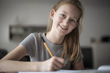 Smiling girl learning at home, writing in exercise book - DKOF00008