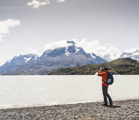 Mann mit Blick auf den Grey Glacier durch ein Fernglas im Torres Del Paine National Park, Patagonien, Chile, Südamerika - UUF20821