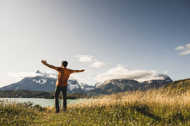 Man with arms outstretched standing at Lake Pehoe in Torres Del Paine National Park, Chile Patagonia, South America - UUF20836