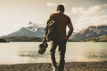 Mann mit Rucksack und Schuhen beim Spaziergang am Pehoe-See im Torres Del Paine National Park Patagonien, Südamerika - UUF20845