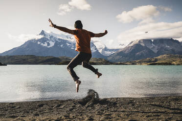 Man with arms outstretched jumping at Lake Pehoe in Torres Del Paine National Park Patagonia, South America - UUF20847