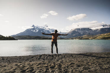 Man with arms outstretched standing at Lake Pehoe in Torres Del Paine National Park Patagonia, South America - UUF20850