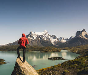 Mann in Kapuzenjacke steht auf einem Felsen am Pehoe-See im Torres Del Paine-Nationalpark, Chile Patagonien, Südamerika - UUF20856