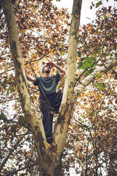 Niedriger Blickwinkel eines jungen Mannes, der wegschaut, während er auf einem Baumstamm steht - EHF00712