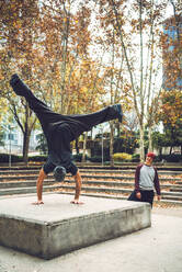 Rear view of male performing handstand by friend in park - EHF00717