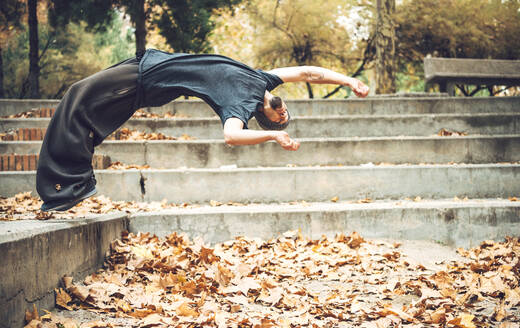 Junger Mann springt über Herbstblätter in einem öffentlichen Park - EHF00728