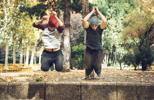 Männliche Freunde springen im Herbst in einem öffentlichen Park - EHF00730