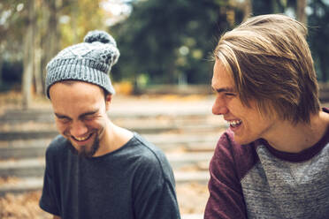 Fröhliche männliche Freunde, die im Park sitzen und sich amüsieren - EHF00739