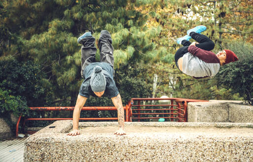 Young man performing handstand while friend jumping in park - EHF00740