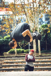 Man with arms crossed looking at friend jumping in park - EHF00749