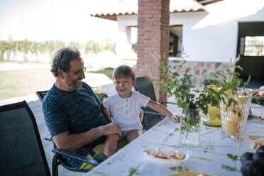 Grandfather and grandchild sitting on chair at dinning table outside house - GRCF00304