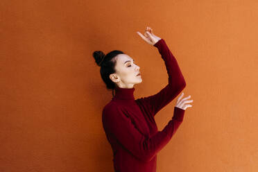 Frau mit geschlossenen Augen tanzt gegen orangefarbene Wand - TCEF00960