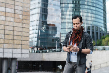 Trendy man text messaging through smart phone while standing in city - JMPF00287