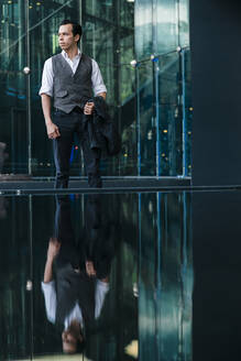 Businessman reflecting on glass while standing outside office building in city - JMPF00297