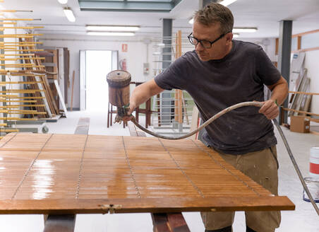 Handwerker beim Auftragen von Lack auf eine Holzjalousie mit Airbrush in einer Tischlerei - ADSF09426