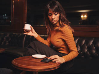 Smart woman surfing mobile phone comfortably sitting at round table and surfing mobile phone - ADSF09429