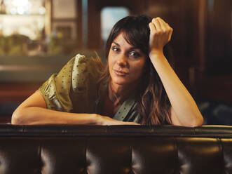 Side view of tired relaxed woman leaning on back of leather black sofa and looking at camera in cafe - ADSF09438