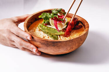 Crop hand of faceless woman holding wooden chopsticks while eating Asian noodle bowl - ADSF09452