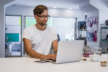 Male student using laptop at kitchen island in cooking class - DLTSF01017