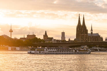 Deutschland, Nordrhein-Westfalen, Köln, Untergehende Sonne beleuchtet Ausflugsschiff vor der Deutzer Hängebrücke - TAMF02654