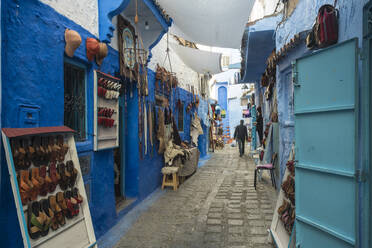 Verschiedene Verkaufsartikel hängen an einer blauen Wand in einer Gasse, Chefchaouen, Marokko - TAMF02674