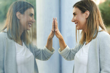 Symmetrical image of smiling businesswoman touching window glass - KIJF03193