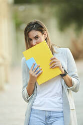 Geschäftsfrau, die ihr Gesicht mit einem Notizbuch bedeckt, während sie im Freien steht - KIJF03195