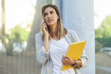 Geschäftsfrau schaut weg, während sie mit einem Mobiltelefon spricht - KIJF03201