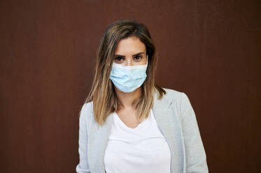 Businesswoman wearing face mask against brown wall - KIJF03204