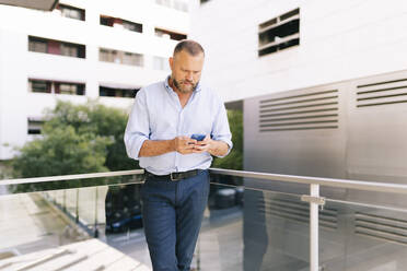 Businessman using smart phone while standing at office balcony - DGOF01192