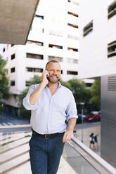 Geschäftsmann, der auf dem Balkon eines Büros steht und mit seinem Handy telefoniert - DGOF01193
