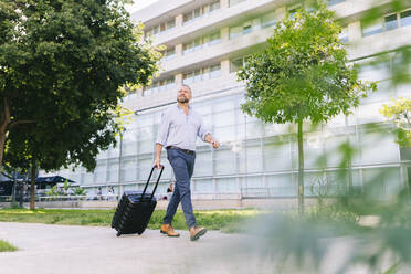 Businessman walking with wheeled luggage at office park - DGOF01200