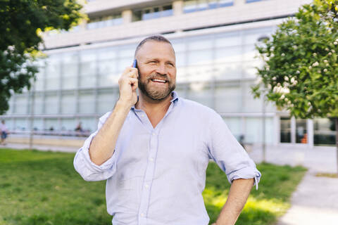 Smiling businessman looking away while talking on mobile phone at office park stock photo