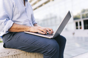 Geschäftsmann, der einen Laptop benutzt, während er im Büropark sitzt - DGOF01205