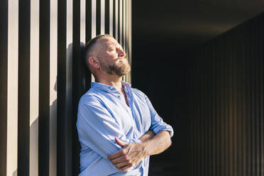 Businessman with arms crossed leaning on wall - DGOF01209