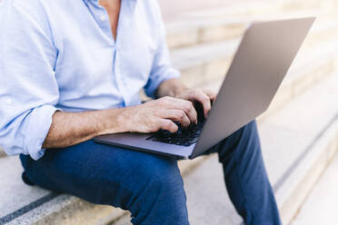 Geschäftsmann arbeitet am Laptop, während er auf einer Treppe sitzt - DGOF01219