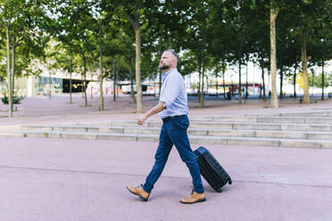 Businessman walking with suitcase in office park - DGOF01221