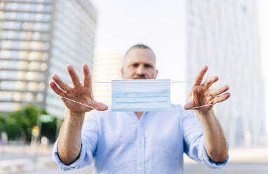 Businessman holding protective face mask in city during COVID-19 - DGOF01225