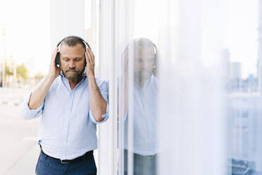 Geschäftsmann hört Musik über Kopfhörer, während er an einem Gebäude vorbeigeht - DGOF01227