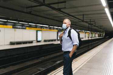 Businessman wearing face mask while standing at subway platform - DGOF01232