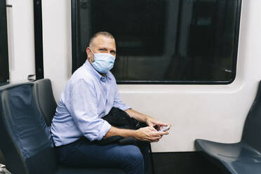 Businessman wearing face mask while traveling in subway train during COVID-19 - DGOF01236