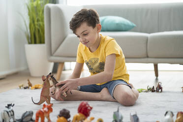 Lächelnder Junge spielt mit Spielzeugtieren im Wohnzimmer zu Hause - SNF00448